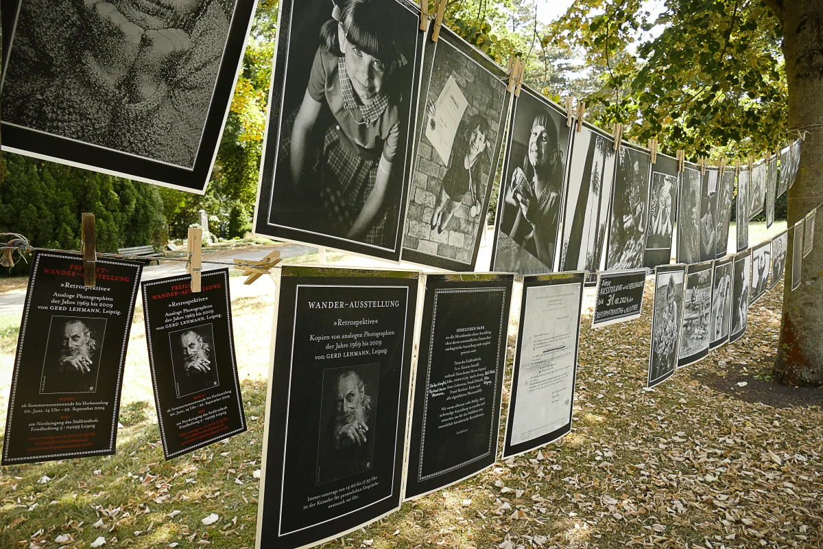 Diverse Fotoabzüge des Fotografen Gerd Lehmann hängen auf zwischen zwei Bäumen gespannten Leinen. Ebenso sind ein Bild des Fotografen und ein einführender Text zu sehen.