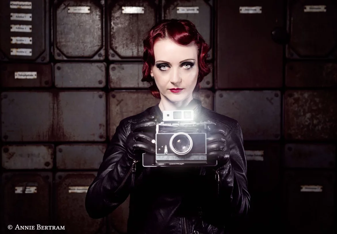 Daniela Vorndran, komplett in Leder gekleidet und eine alte Kamera in Händen halten. Das Make-Up und die Frisur erinnern an die 20- und 30er Jahre. Das Foto wurde von Annie Bertram angefertigt.