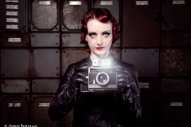 Daniela Vorndran, komplett in Leder gekleidet und eine alte Kamera in Händen halten. Das Make-Up und die Frisur erinnern an die 20- und 30er Jahre. Das Foto wurde von Annie Bertram angefertigt.