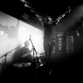 Der Sänger der Band "Zweite Jugend" steht auf der Bassdrum und hebt begeistert die Arme in die Luft. Im Hintergrund lacht der Schlagzeuger der Zwei-Mann-Band.